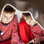 Two kids under a blanket with a flashlight