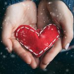 An image of two hands holding a small heart pillow.