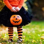 Girl dressed for Halloween, holding a jack-o-lantern bucket.