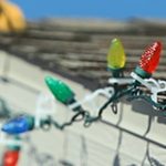 Person hanging holiday lights on their roof