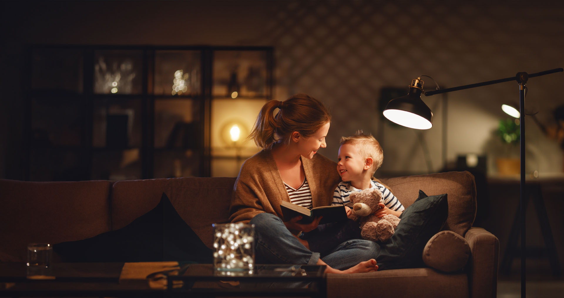 Mom and young son reading a book by lamp light on the couch