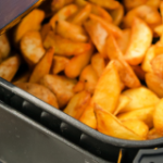 A hand holding the basket to an air fryer containing shredded chicken and buffalo sauce.