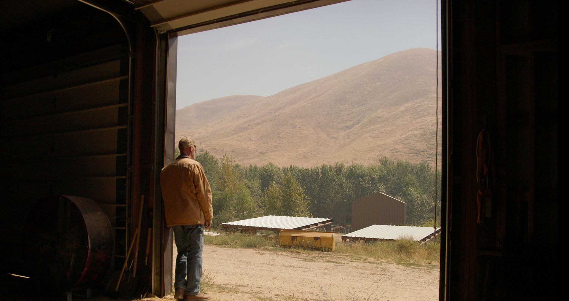 Farmer standing against doorway of a barn, looking outside